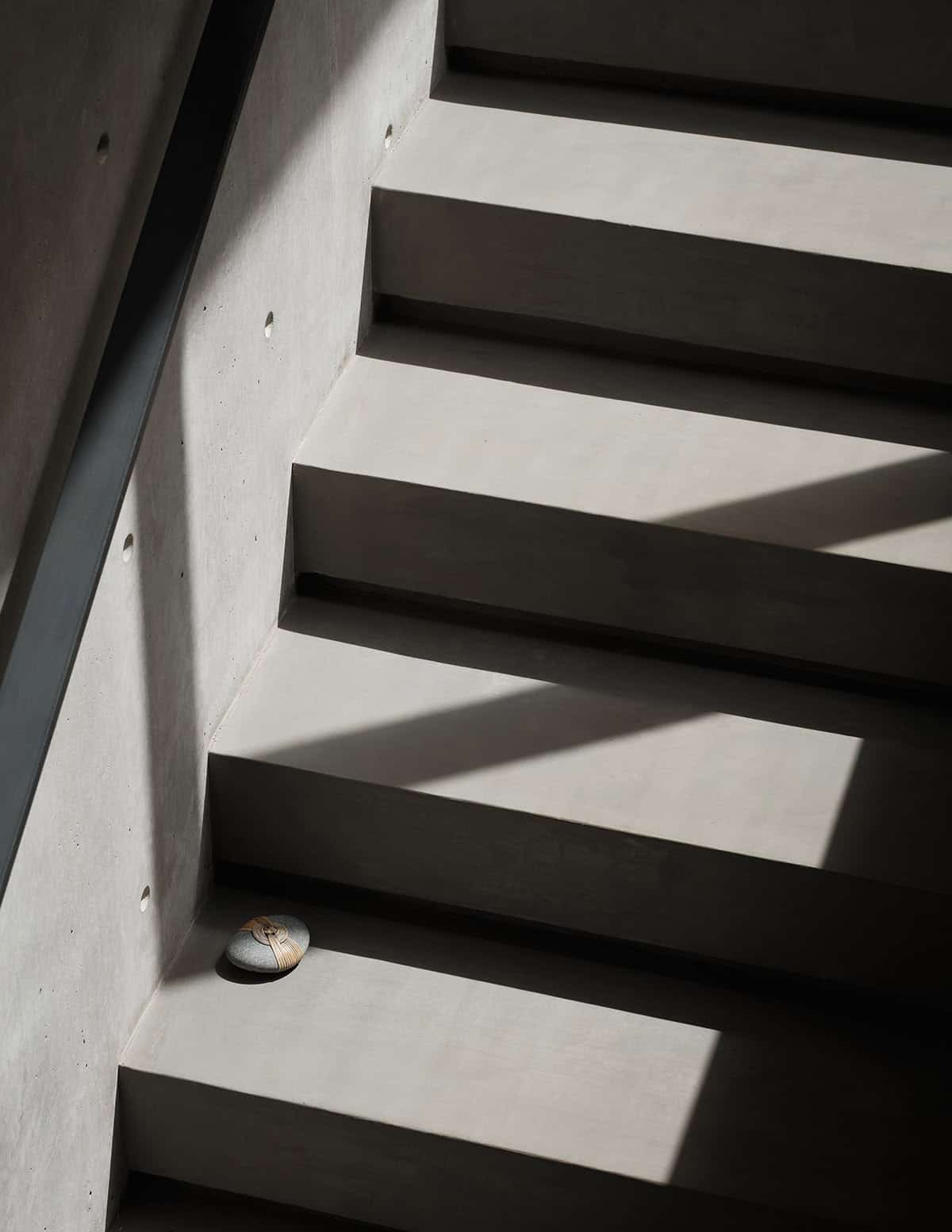 Concrete exterior stairs with dramatic diagonal shadow and a single stone on a tread