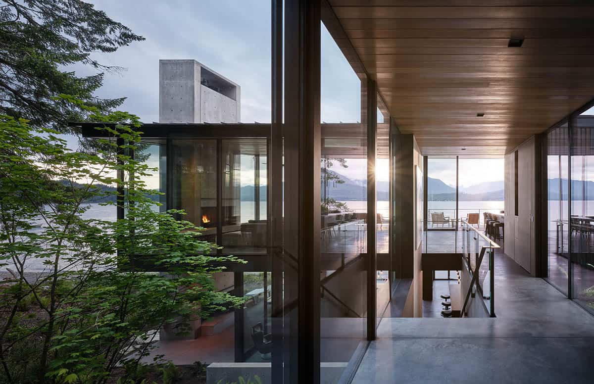 Upper-level interior bridge with cedar ceiling overlooking the living room fireplace and sunlit mountain lake beyond