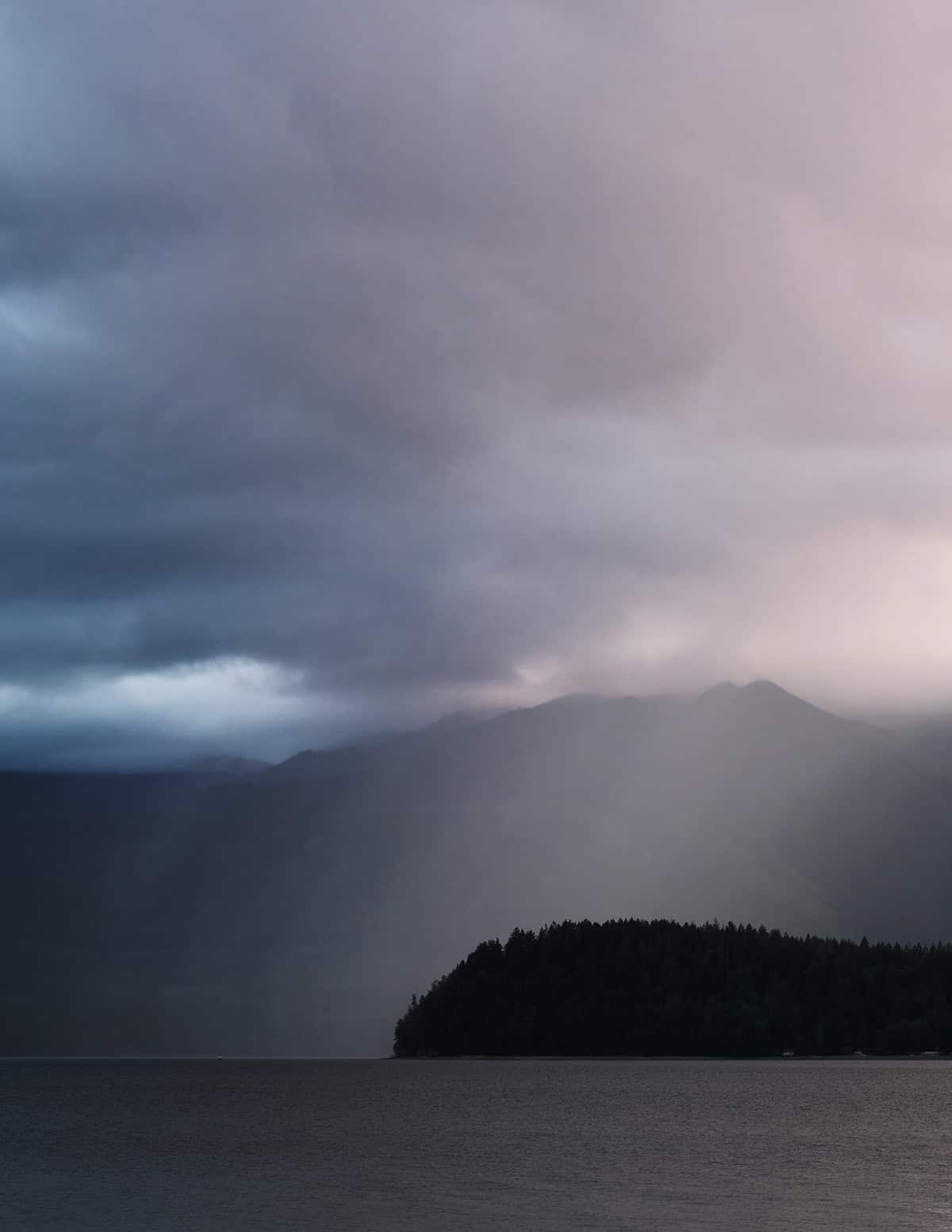 Dramatic stormy dusk over a mountain lake with rain squall and a forested island silhouette