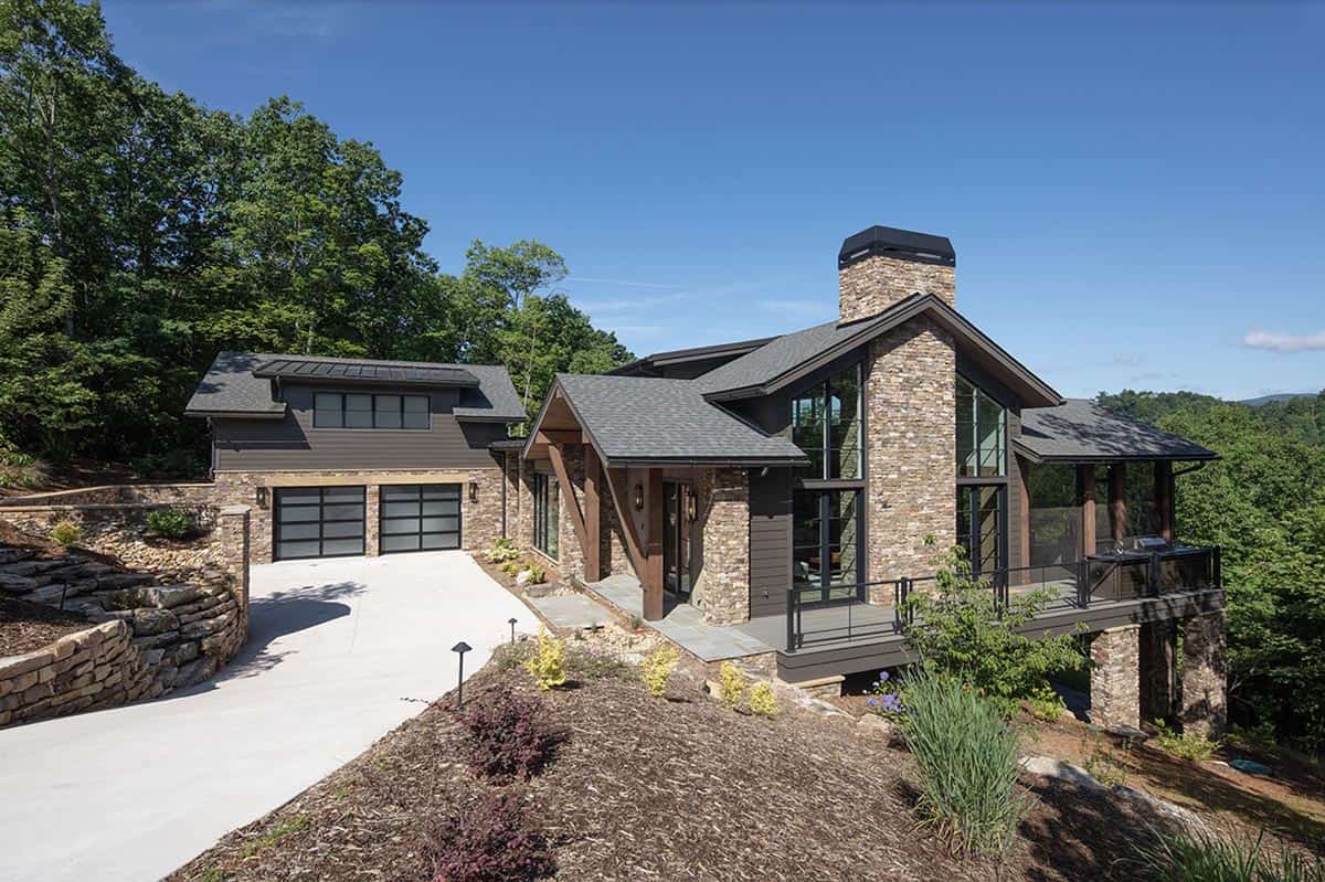 Aerial-angle exterior view showing stone chimney, garage, and cantilevered deck with mountain views