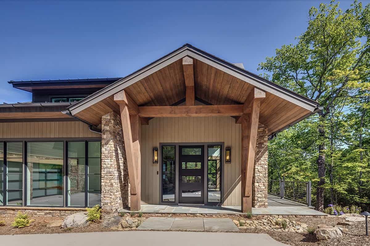 Covered entry portico with exposed timber beams, wood ceiling, and black front door