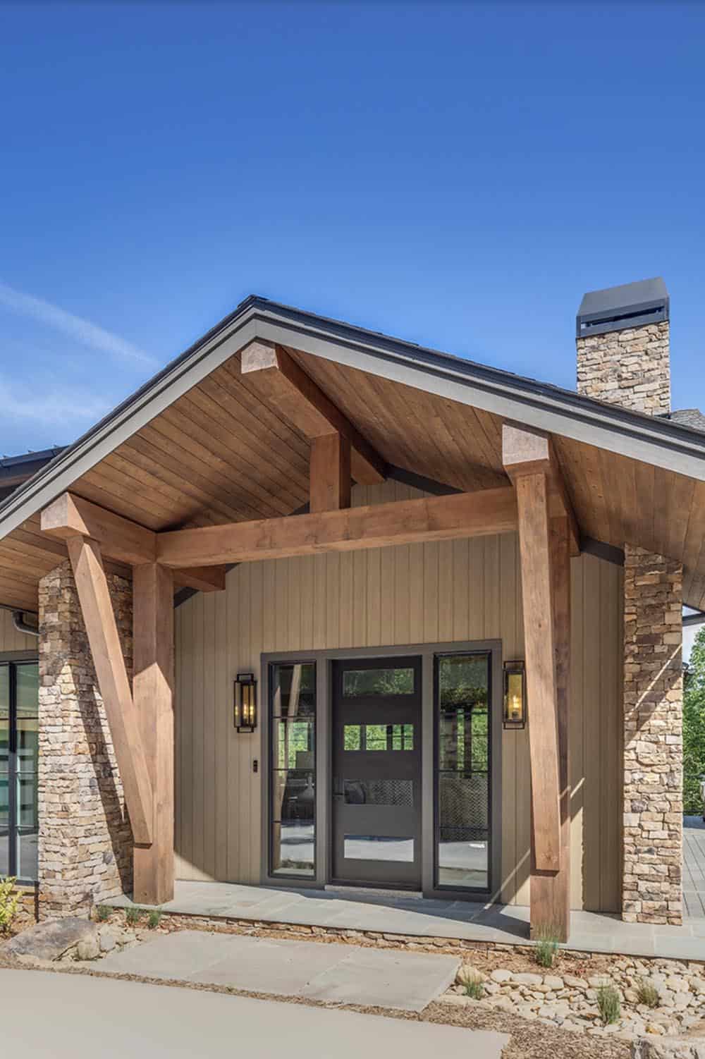Grand timber frame entry with angled wood posts, stone pillars, and double black glass door