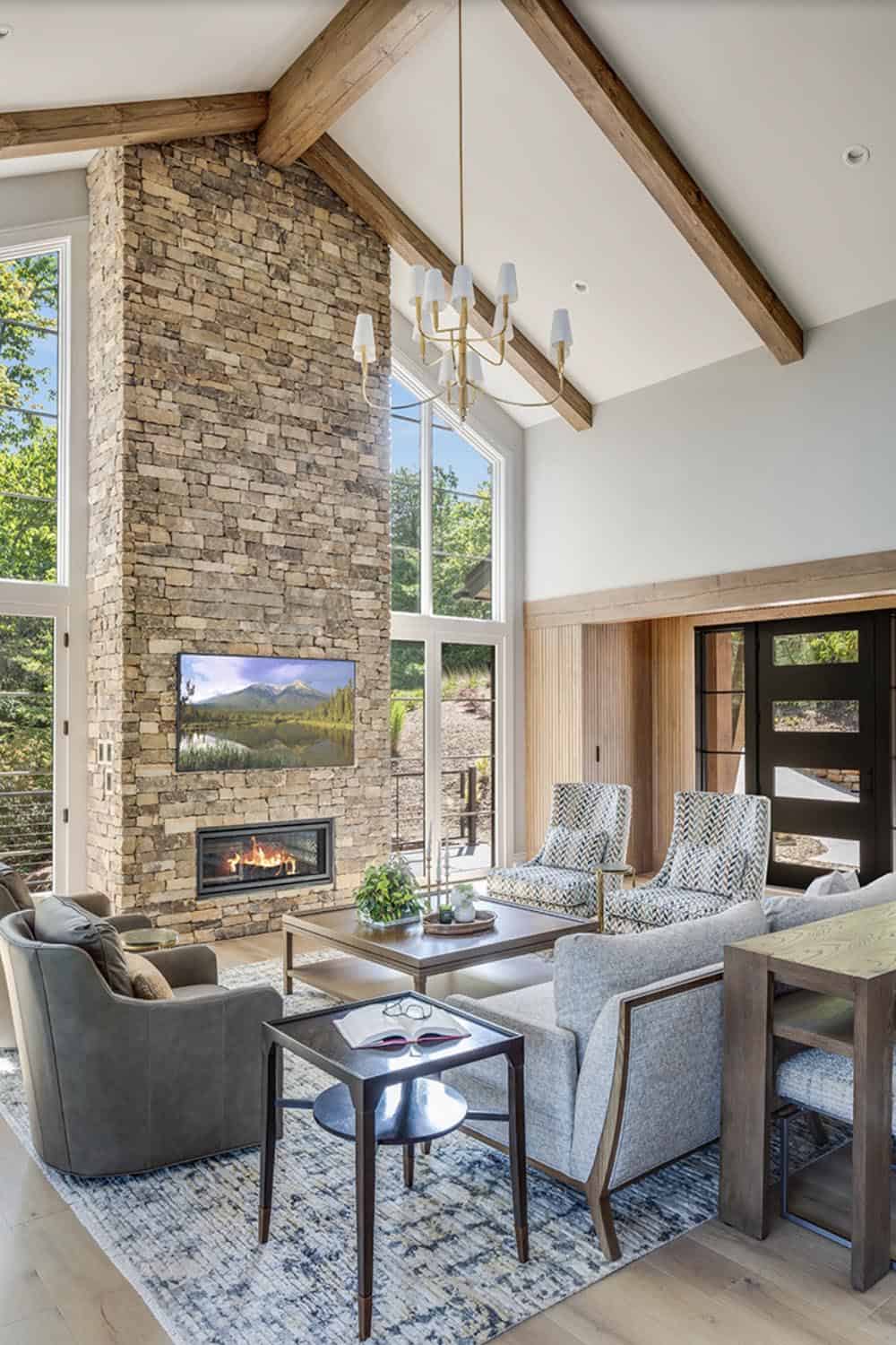 Vaulted great room with floor-to-ceiling stone fireplace, wood ceiling beams, and gold chandelier