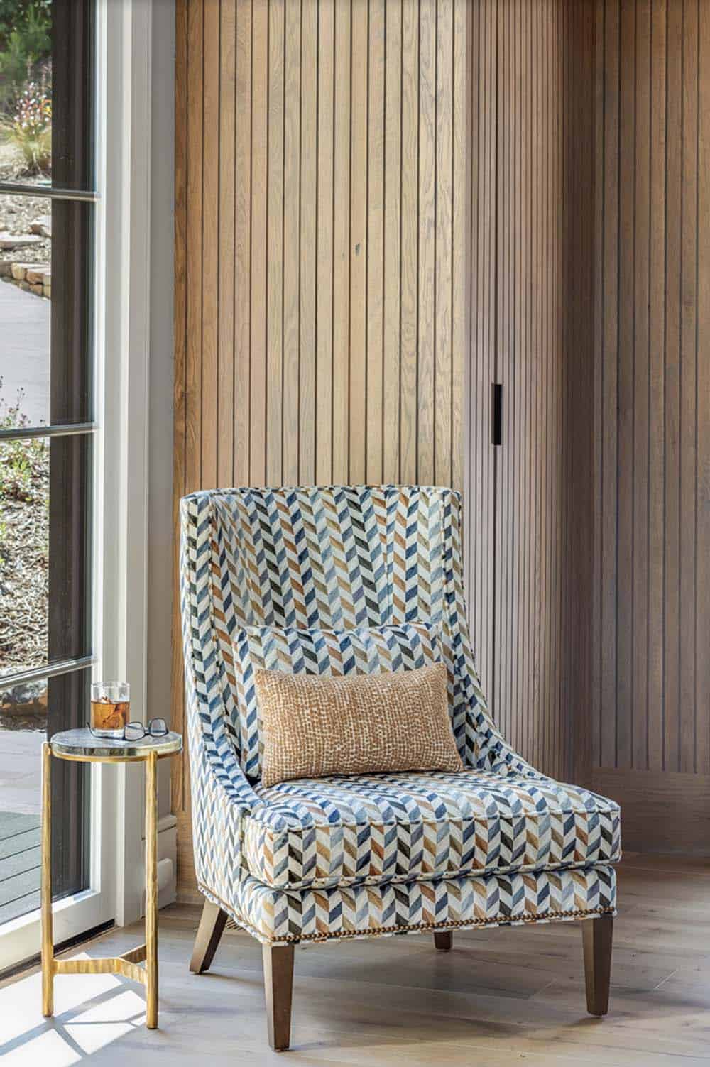 Herringbone-patterned accent chair against vertical wood slat wall panel beside floor-to-ceiling window