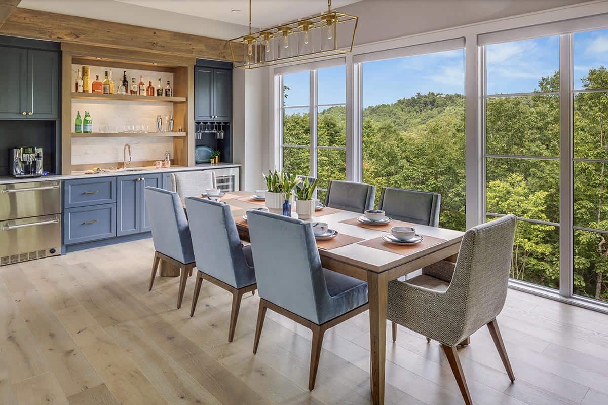 Dining area with walnut table, blue velvet chairs, wet bar, and panoramic mountain forest views