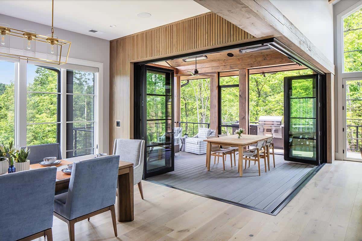 Indoor-outdoor dining space with accordion glass doors open to covered deck and forest canopy