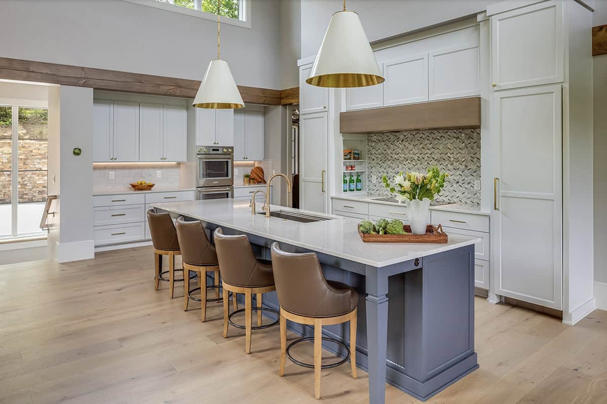 Kitchen with white shaker cabinets, slate-blue island, quartz countertops, and gold pendant lights
