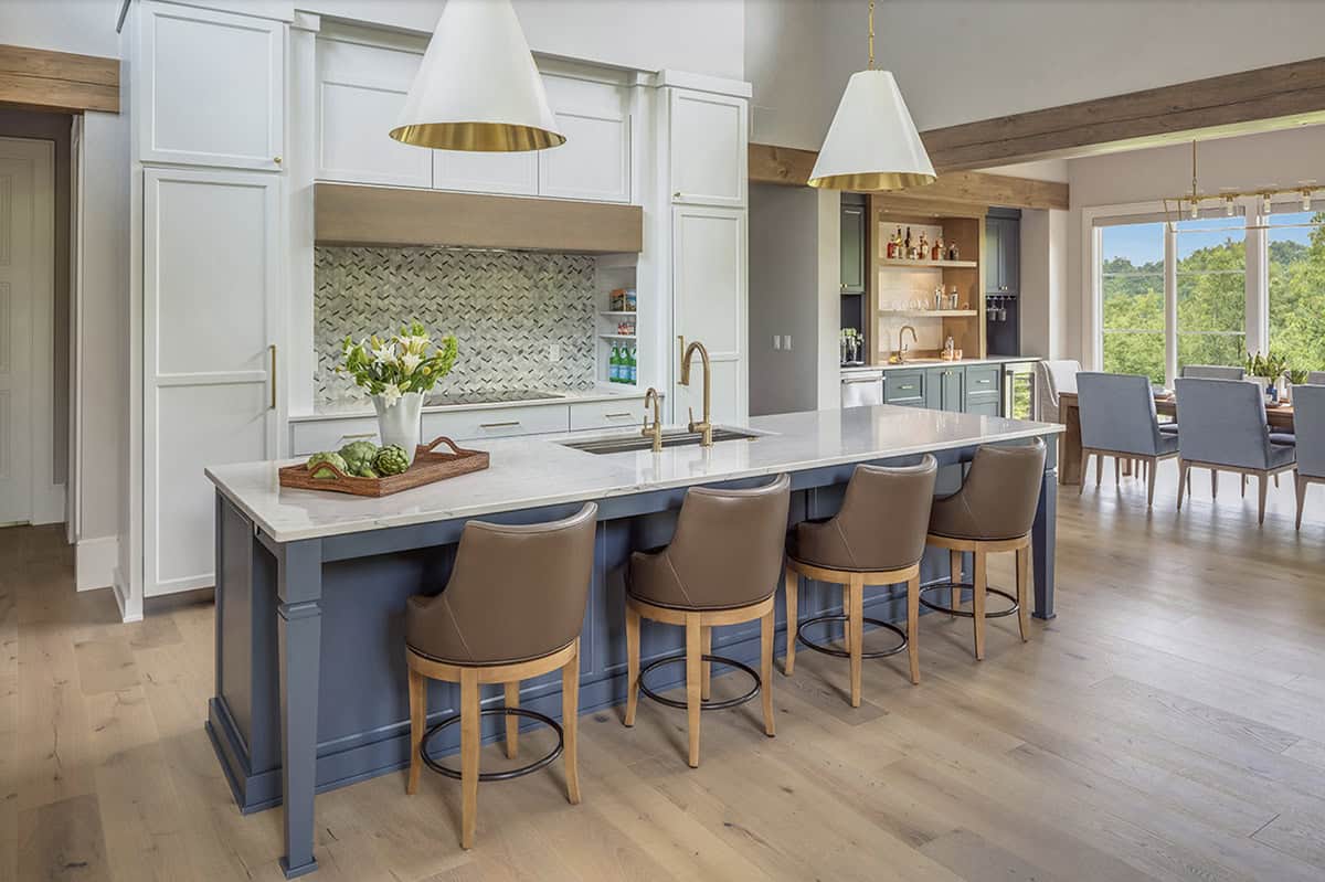 Wide kitchen view showing blue island with leather barstools, mosaic backsplash, and dining area beyond