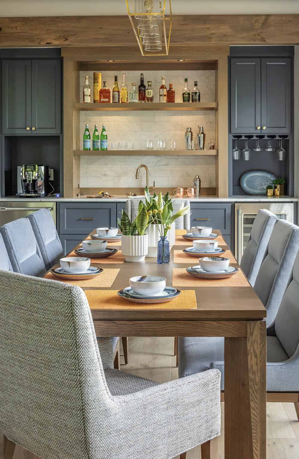Dining room with wood table, mixed gray chairs, and fully stocked built-in bar with marble backsplash