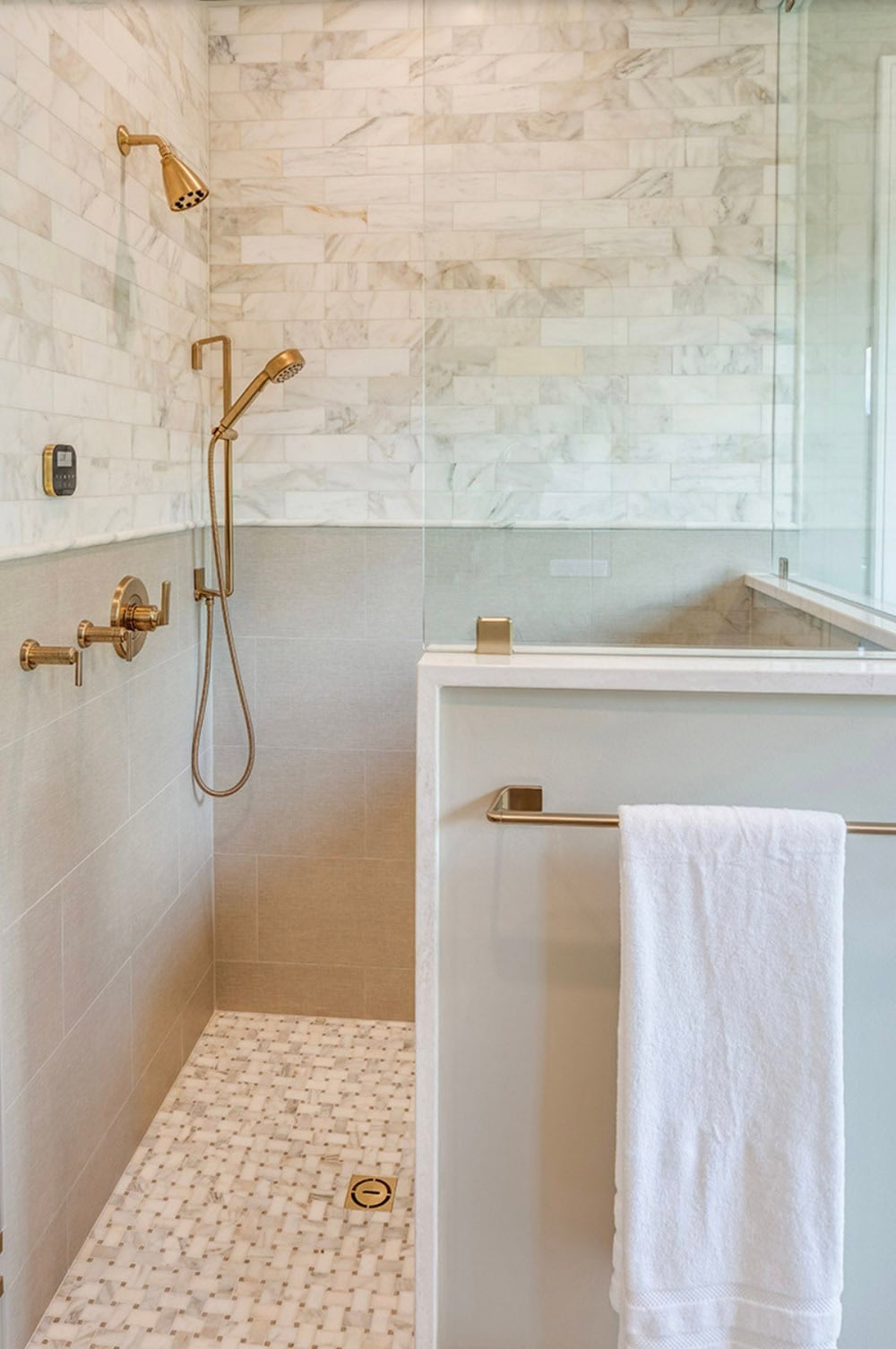 Walk-in shower with marble subway tile, basket weave mosaic floor, and gold rain and hand shower