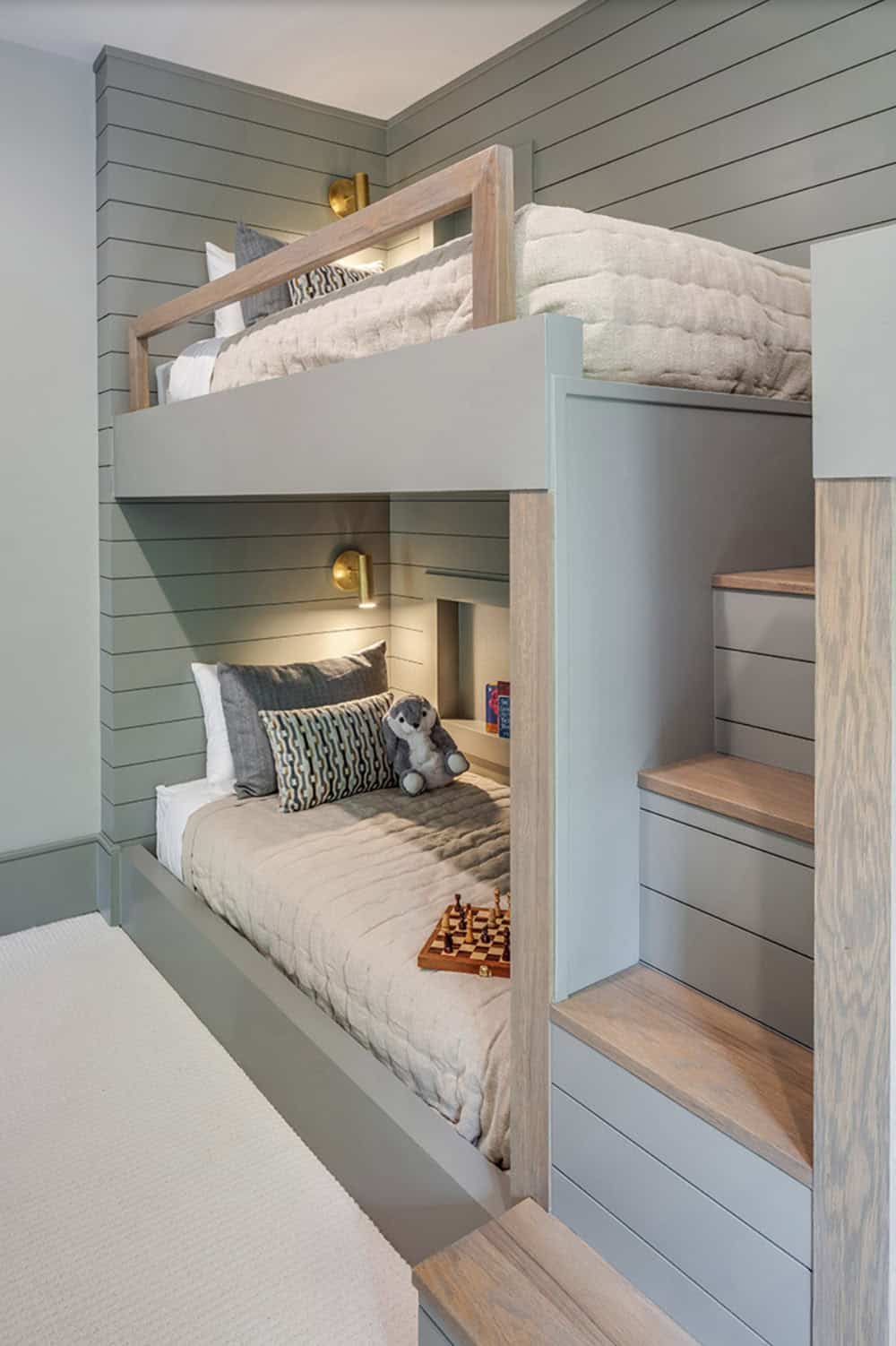 Close-up of built-in bunk bed with wood frame, storage stairs, reading light, and shiplap wall