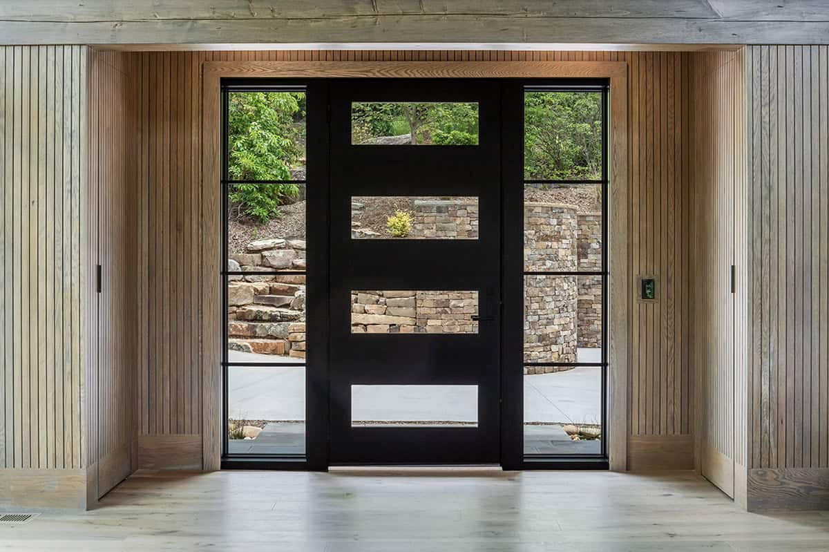 Foyer entry with black glass-panel front door flanked by vertical wood slat walls and sidelights