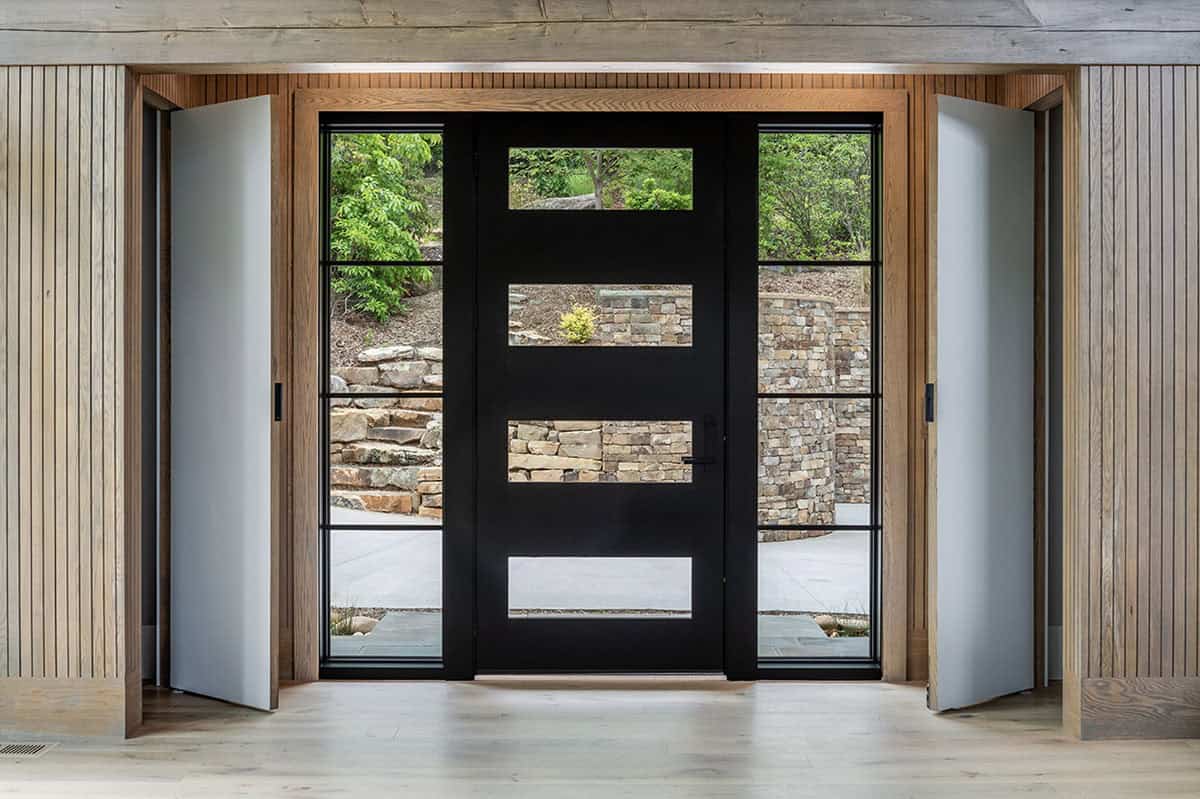 Open foyer showing black front door with sidelights, wood slat walls, and stone retaining wall beyond