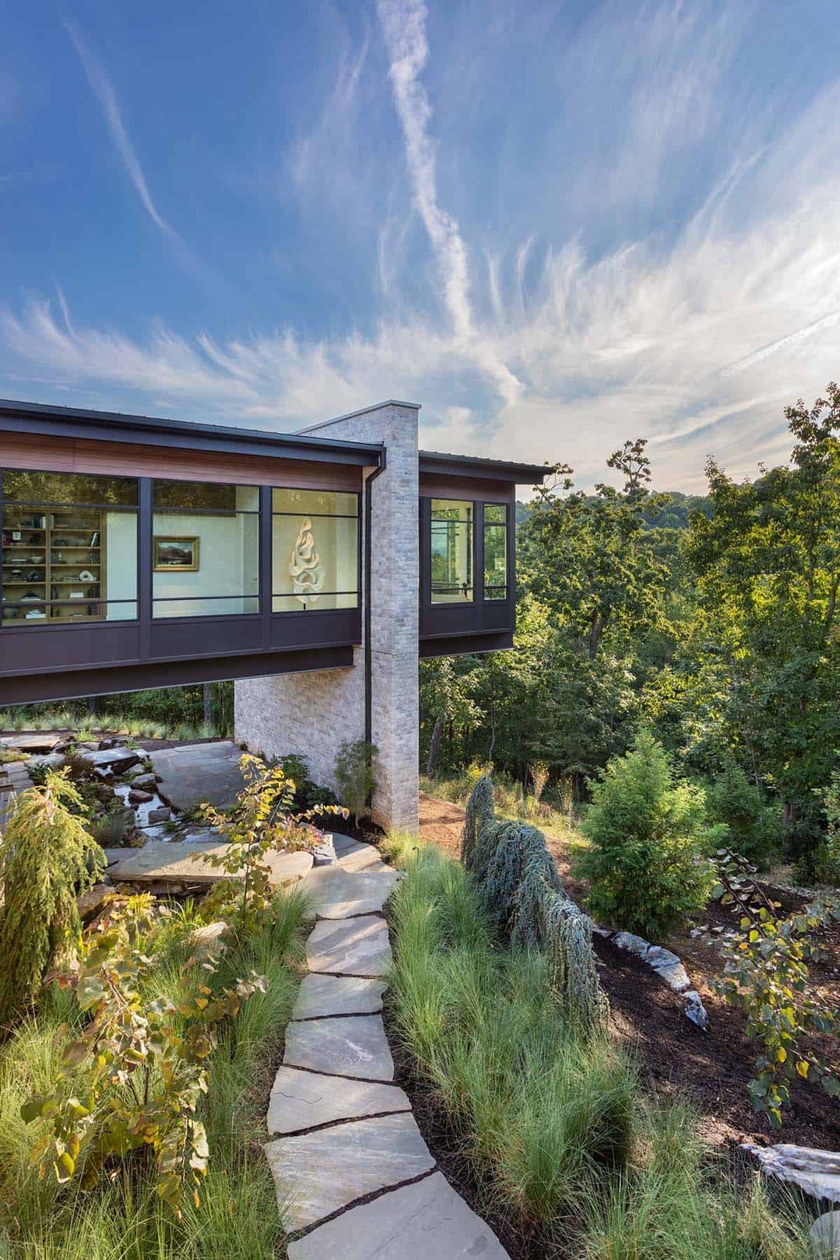 Stone and glass modern home exterior with flagstone path and lush landscaping