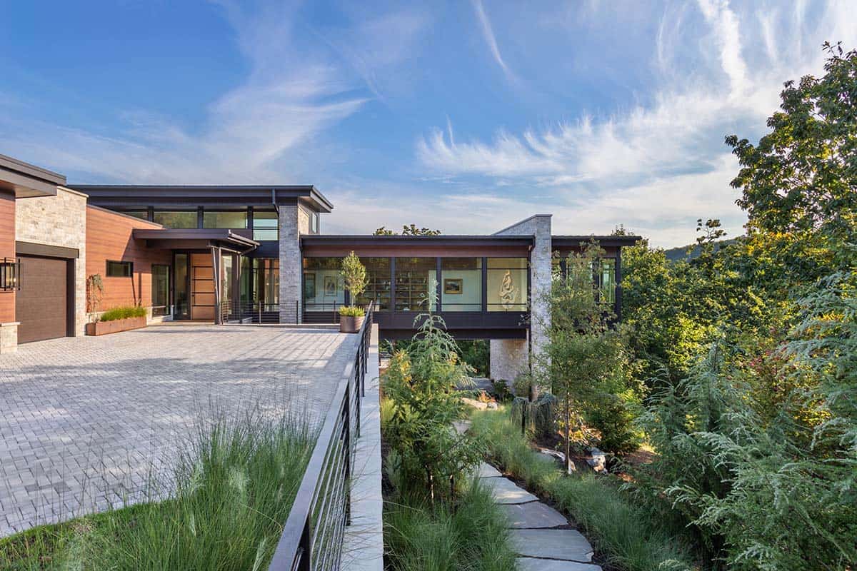 Front elevation of mountain modern home with wood siding, stone columns, and paver driveway