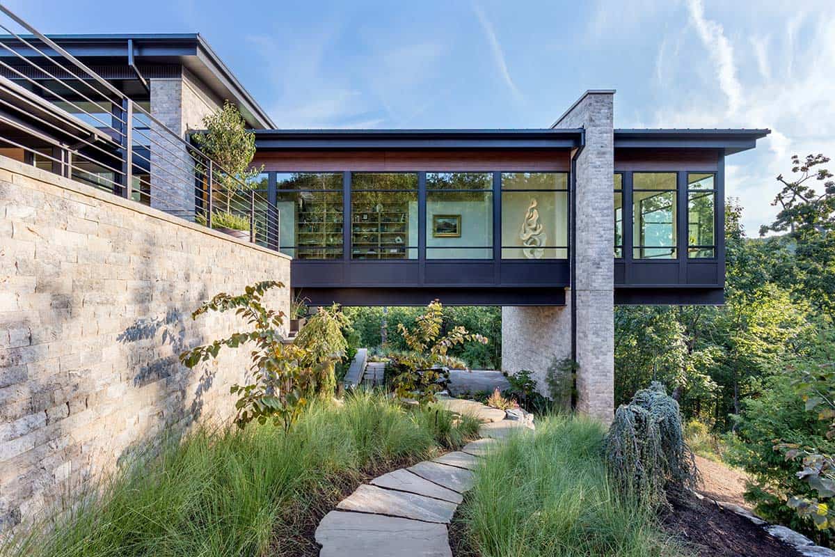 Cantilevered glass bridge connecting stone towers above natural garden pathway