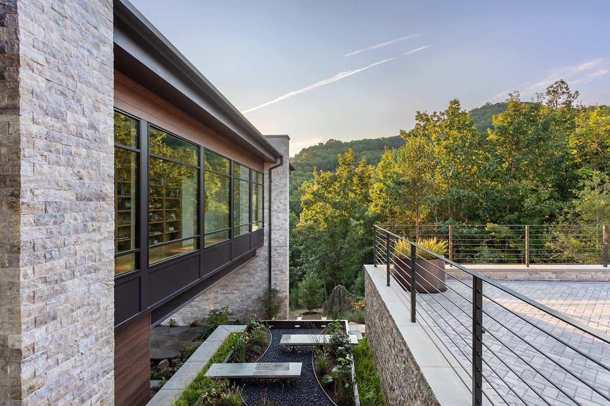 Side view of stone facade with floor-to-ceiling windows overlooking forested valley