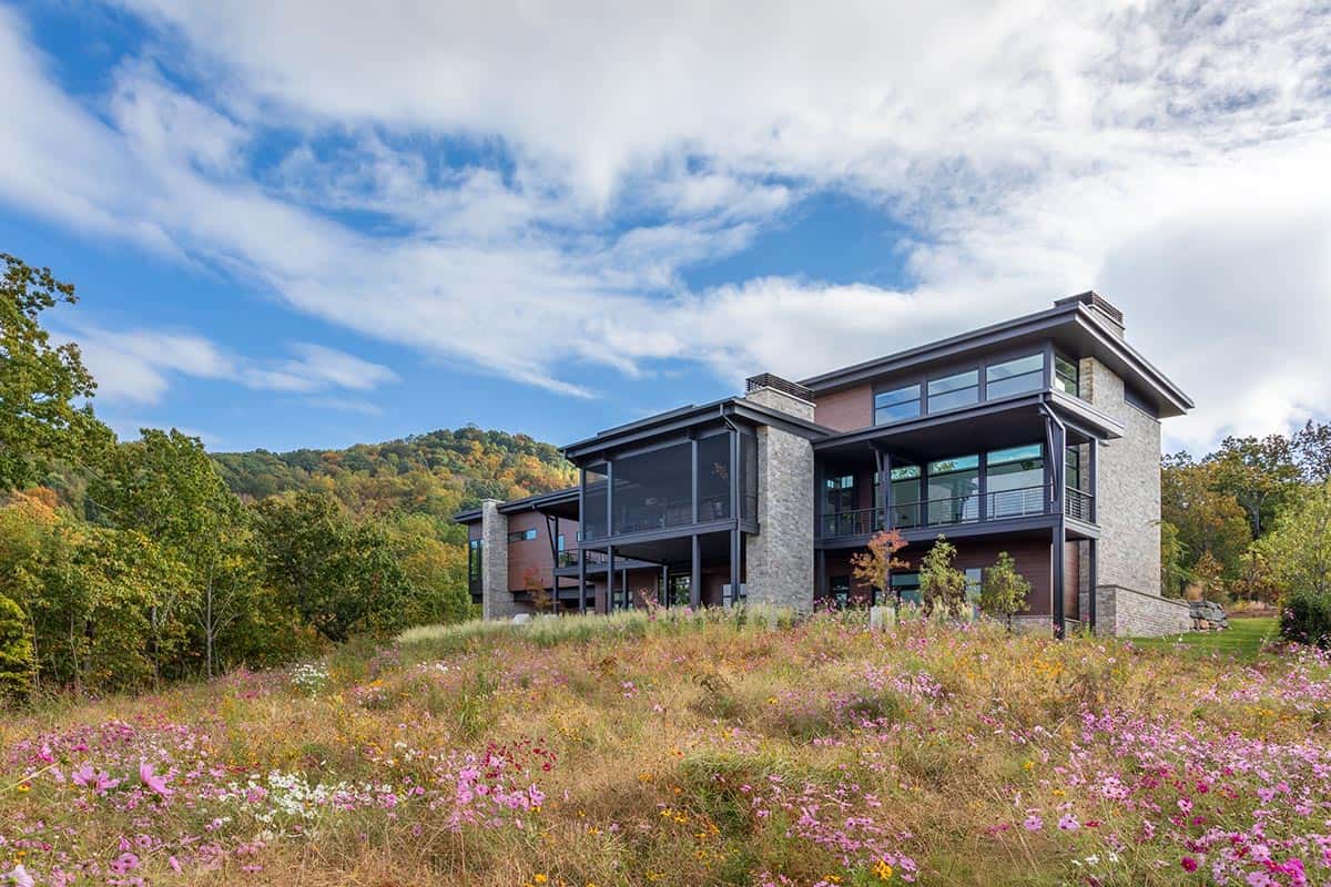 Rear facade of multi-level modern home rising above wildflower meadow in autumn