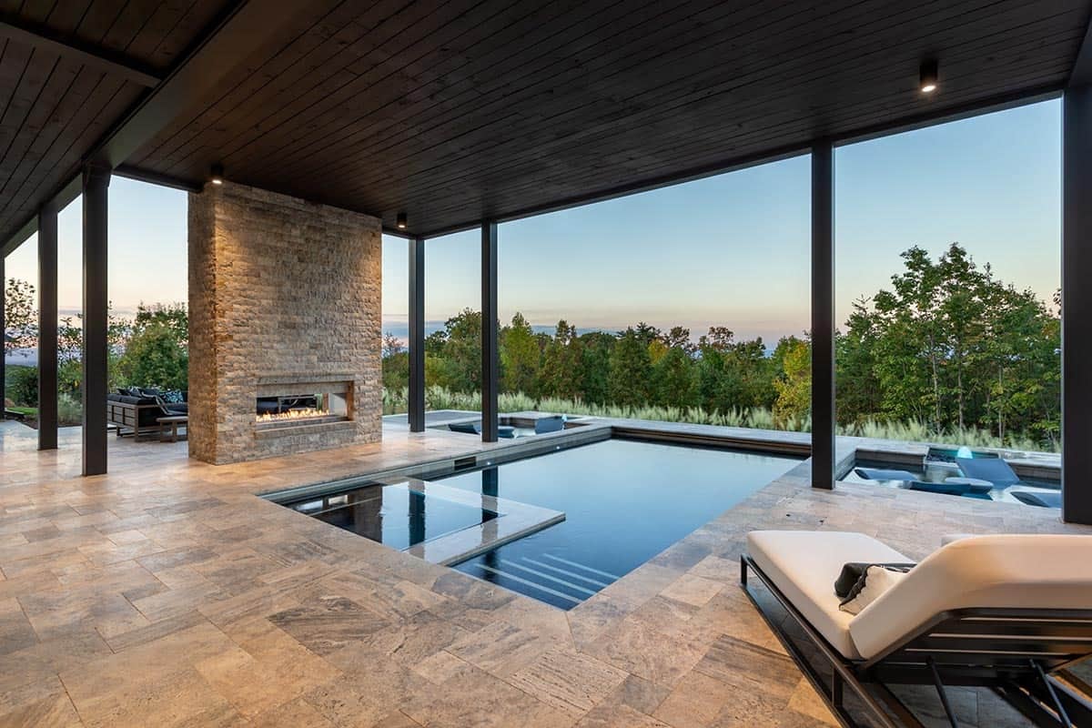 Covered outdoor pool area with stone fireplace and panoramic mountain views at dusk