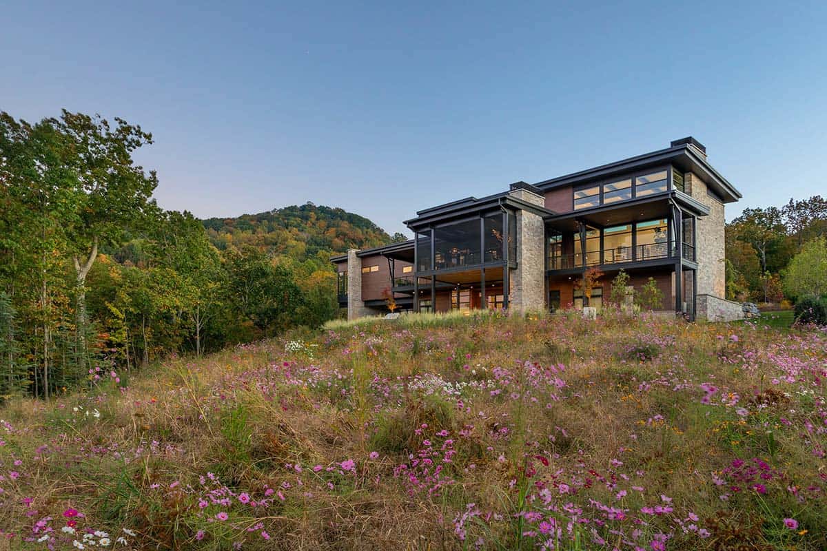 Modern mountain home exterior seen from wildflower field at twilight