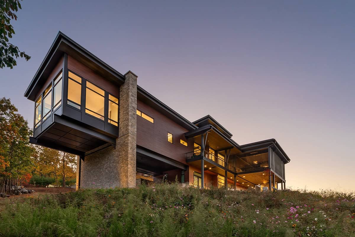 Cantilevered upper level glowing at dusk above sloped meadow garden