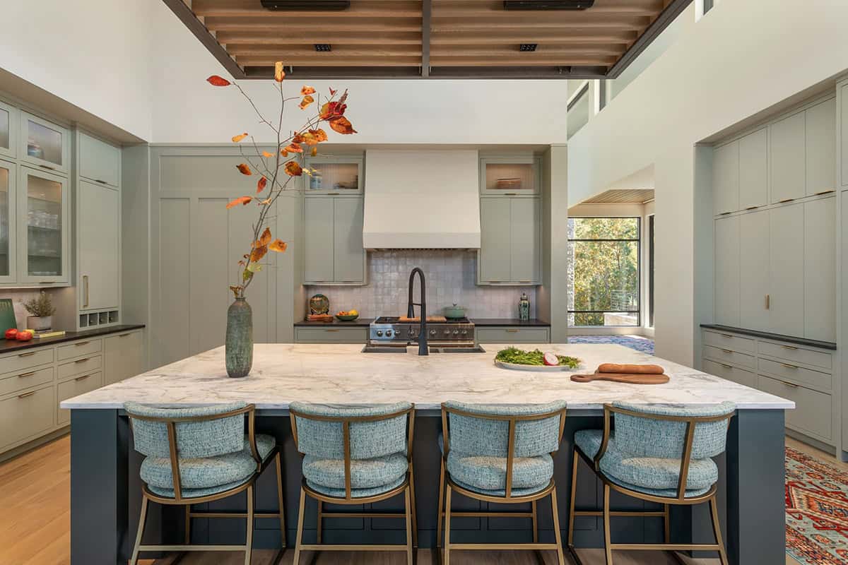 Kitchen with sage green cabinets, marble island, and blue upholstered barstools