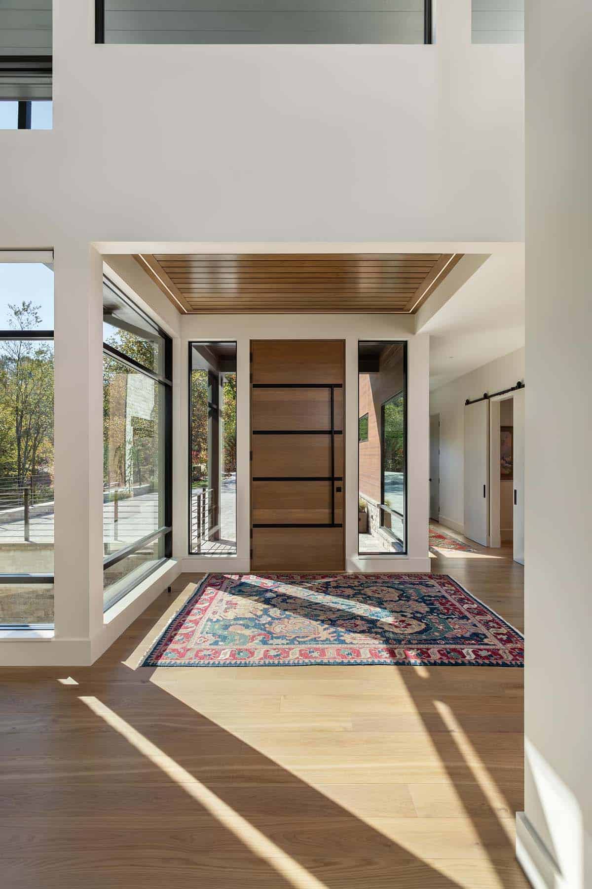 Double-height foyer with wood pivot door, clerestory windows, and Persian rug