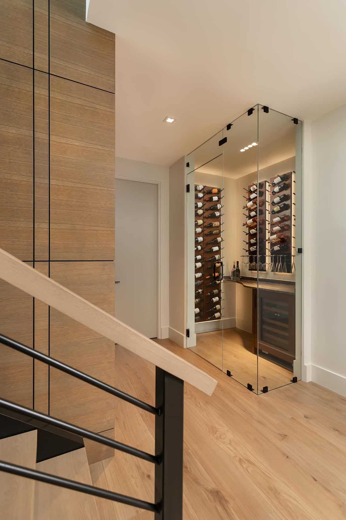 Glass-enclosed wine cellar with wall-mounted bottle racks visible from staircase landing