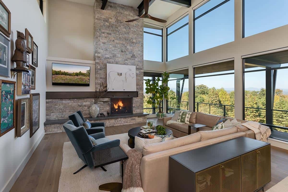 Double-height living room with stone fireplace, gallery wall, and panoramic corner windows