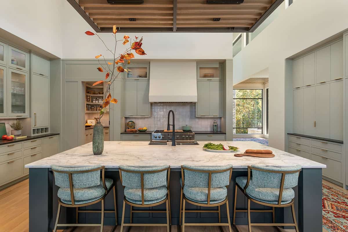 Kitchen with sage green cabinets, marble island, blue barstools, and wood slat ceiling