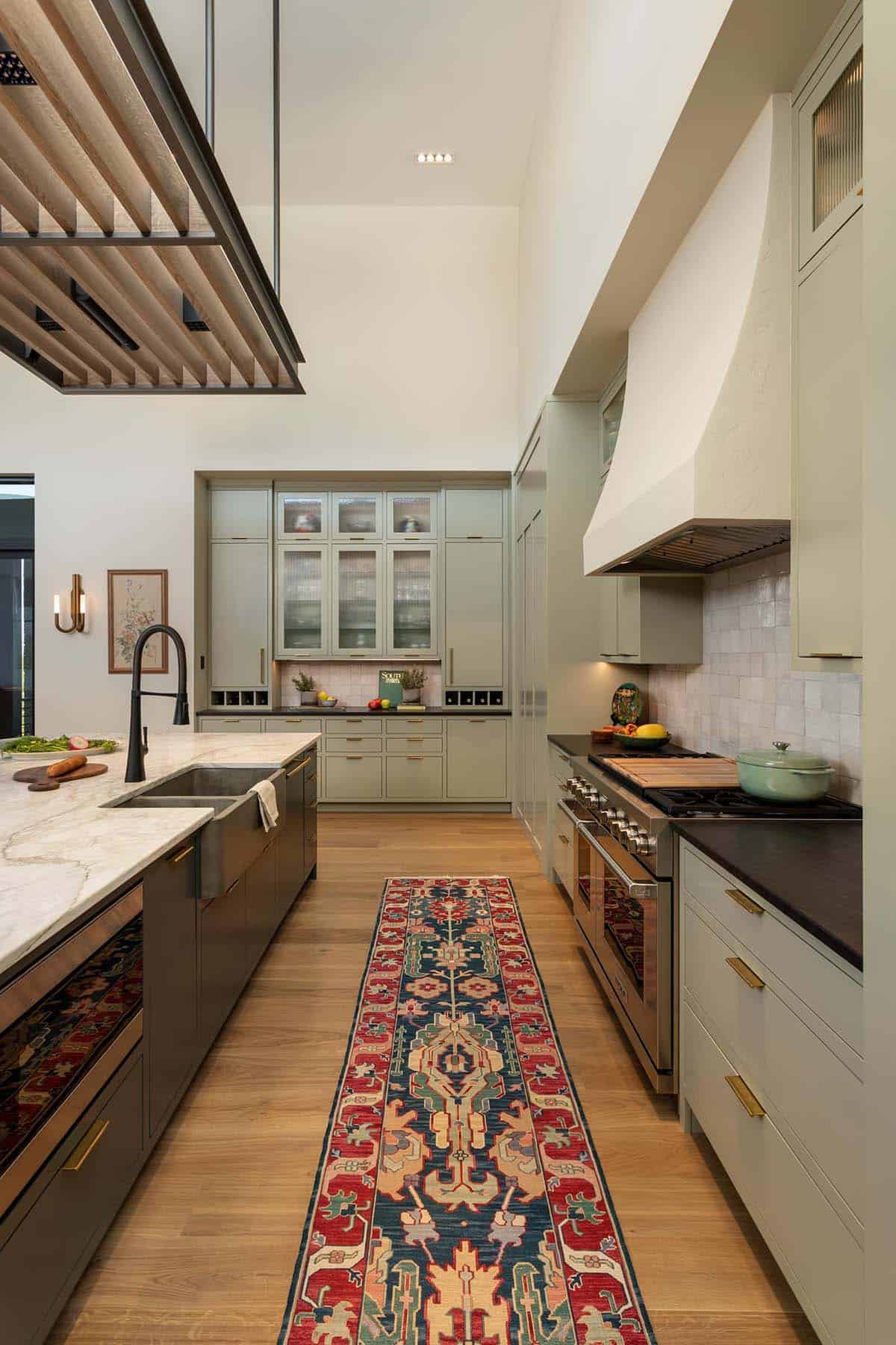 Kitchen with sage green cabinetry, Persian runner, professional range, and white hood
