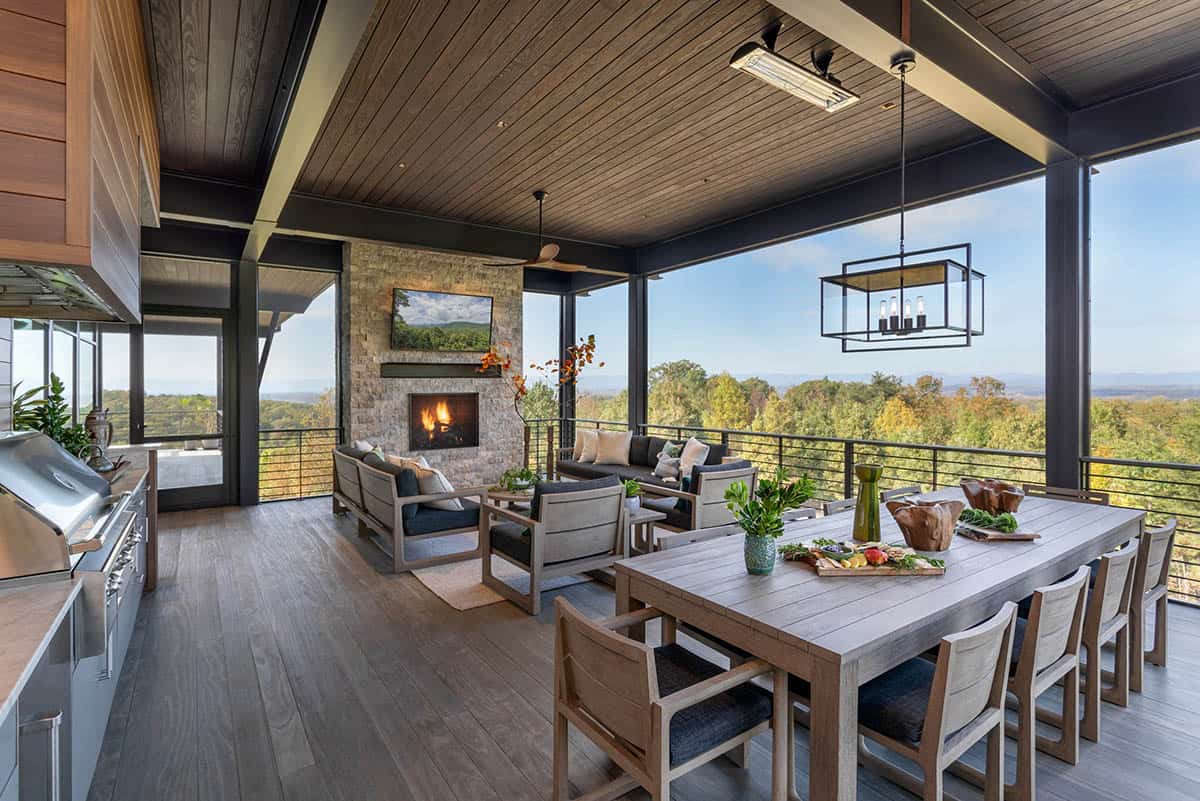 Screened porch with outdoor kitchen, dining table, stone fireplace, and autumn valley views
