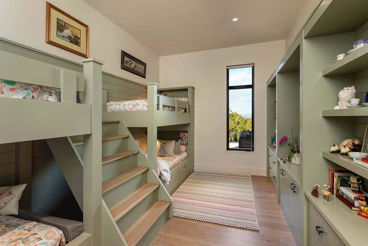 Children's bunk room with sage green built-in bunks, staircase, and open shelving