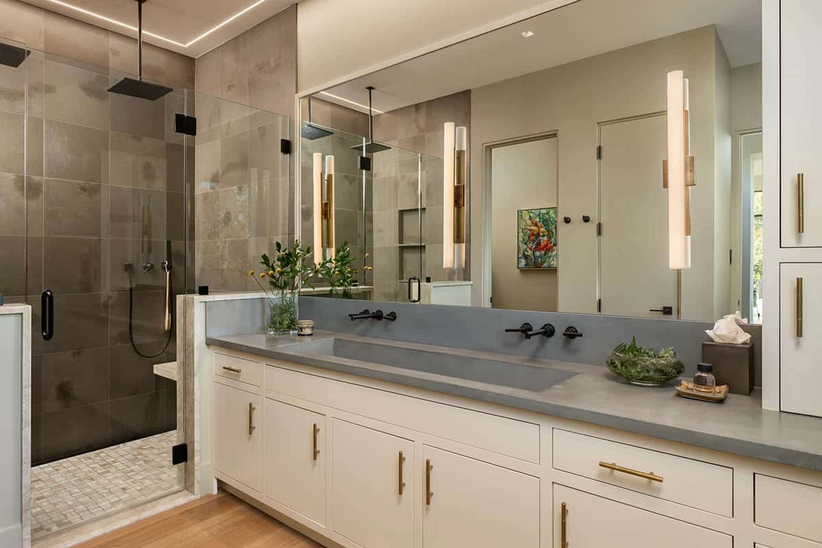 Primary bathroom with long concrete vanity, glass shower, and gold sconce lighting