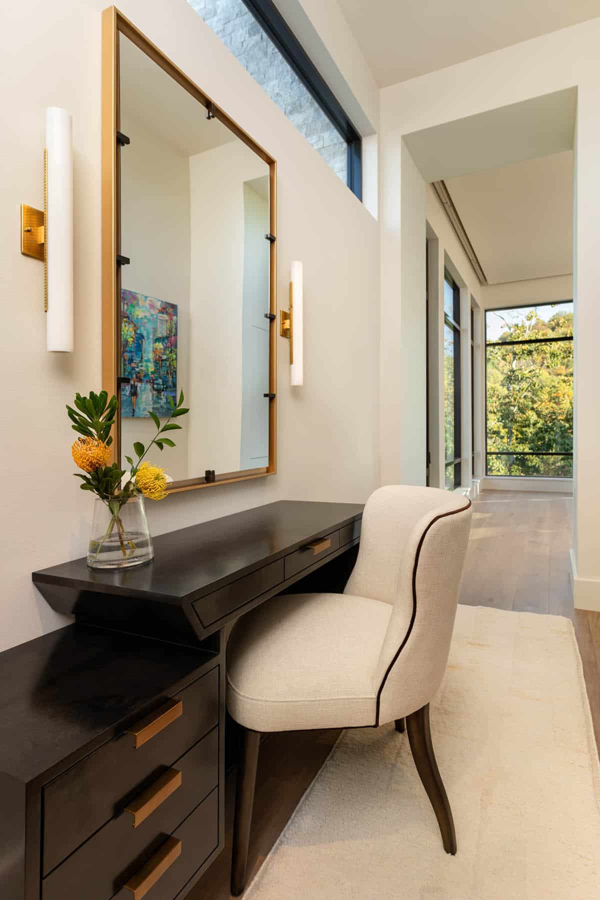Bedroom dressing area with dark wood vanity, gold mirror, and hallway with forest views