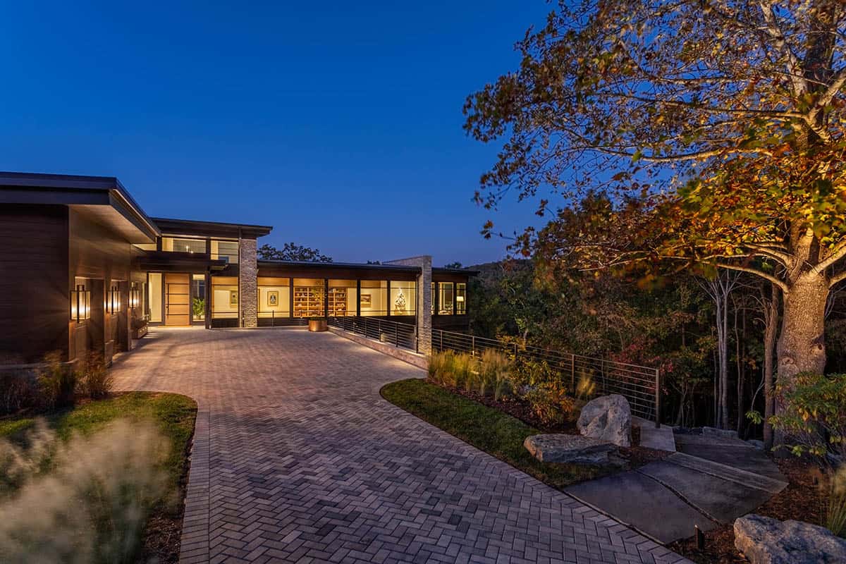 Nighttime front approach with paver driveway, lit interior, and autumn foliage