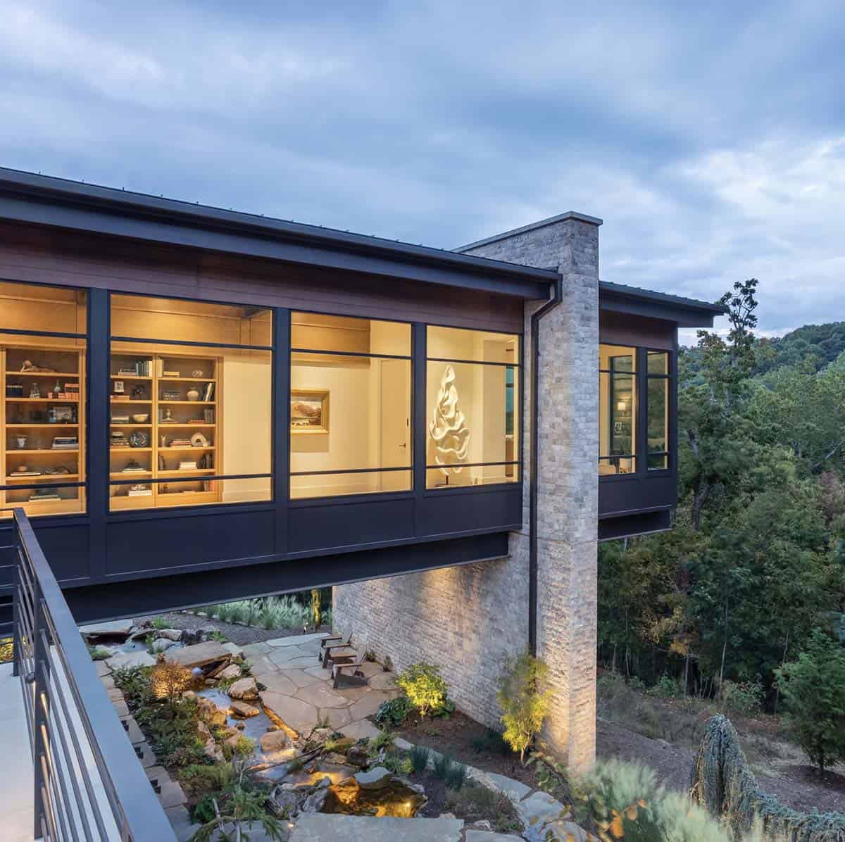 Glowing cantilevered library wing at dusk above lit rock garden and stream