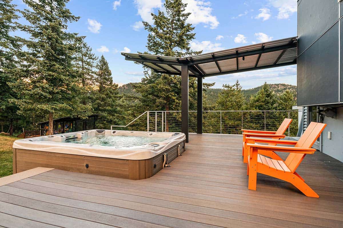 A partially sunken hot tub on a composite deck with bright orange Adirondack chairs and a mountain forest view in Boulder, Colorado