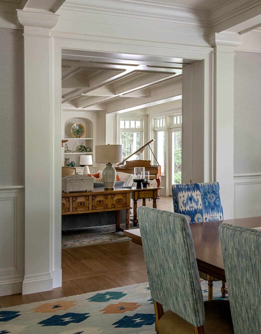 View through paneled archway into sitting room with grand piano and built-in shelving