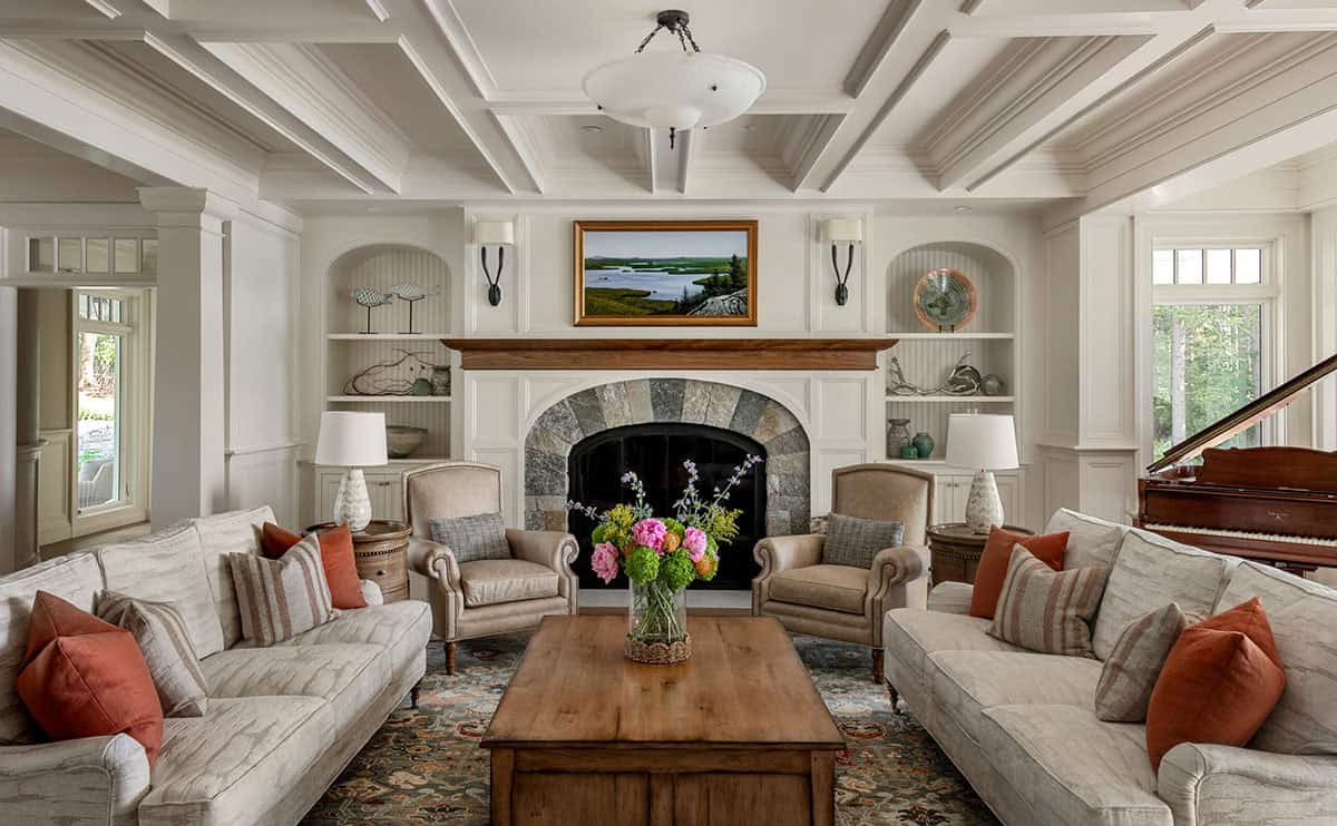 Living room with stone fireplace, coffered ceiling, neutral sofas, and grand piano