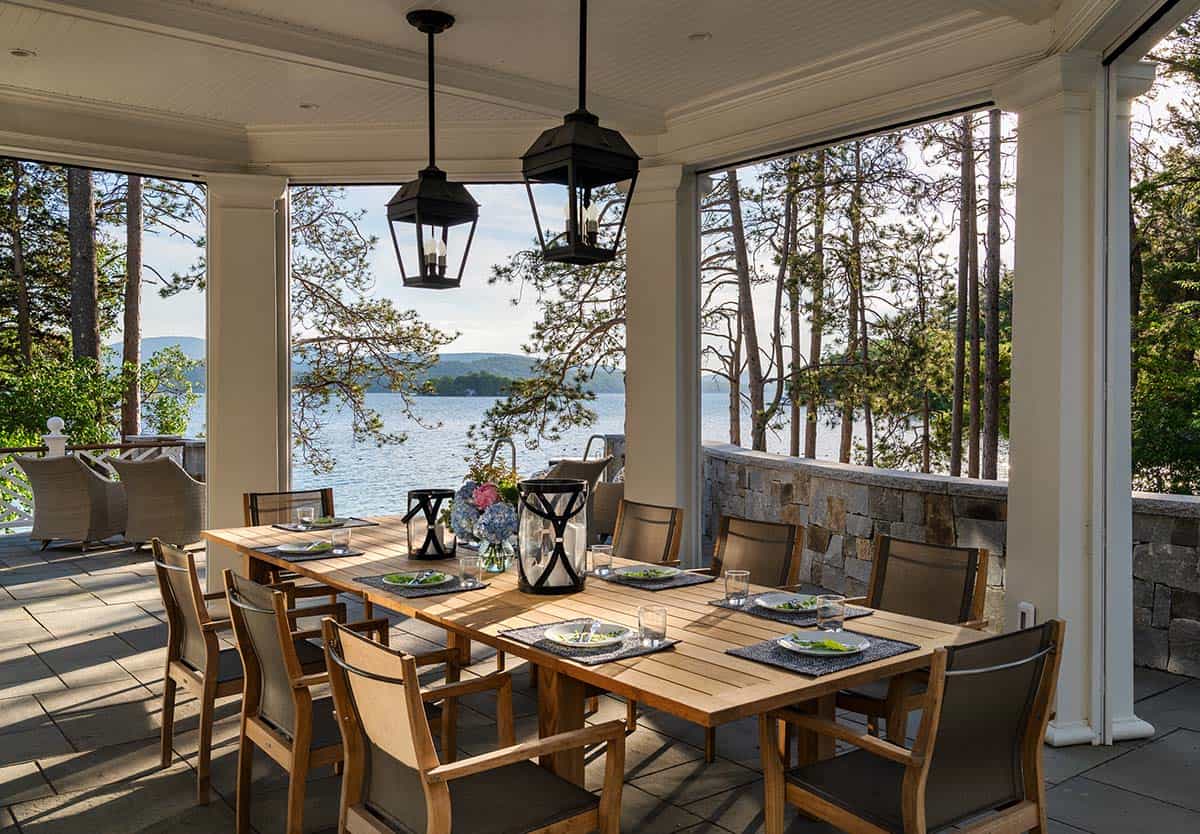 Covered porch dining area with teak table set for eight overlooking the lake