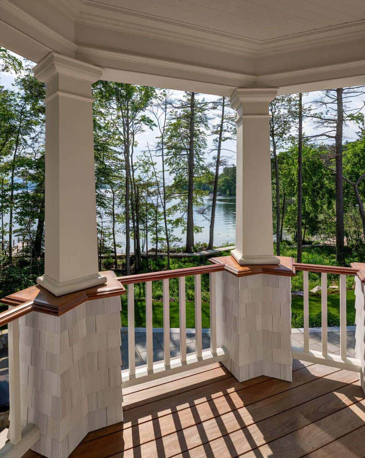 Corner of covered porch with white columns framing a wooded lake view