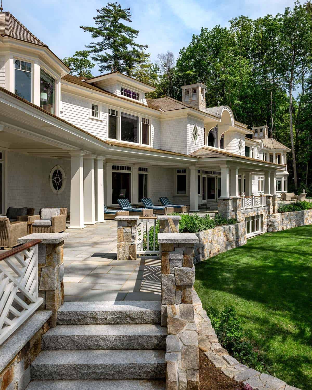 Stone-walled patio with lounge chairs along the home's covered porch and lawn