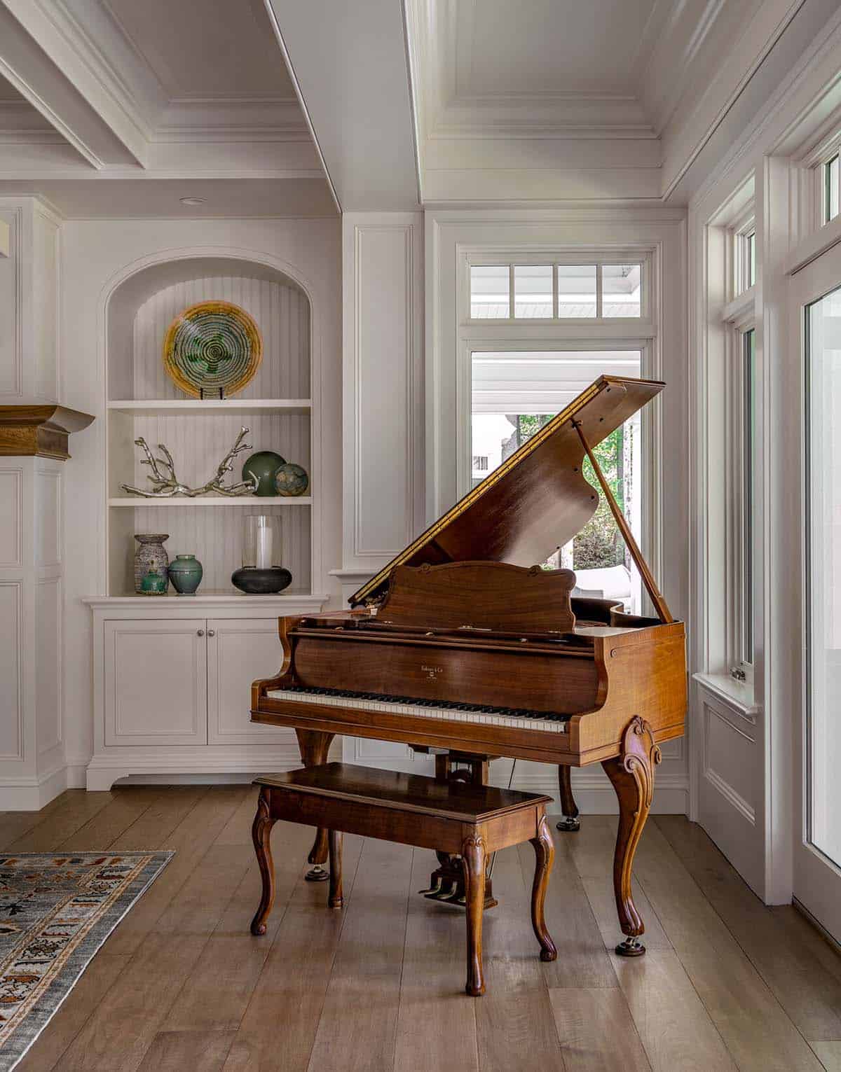 Grand piano in sunroom corner with built-in display shelves and garden views