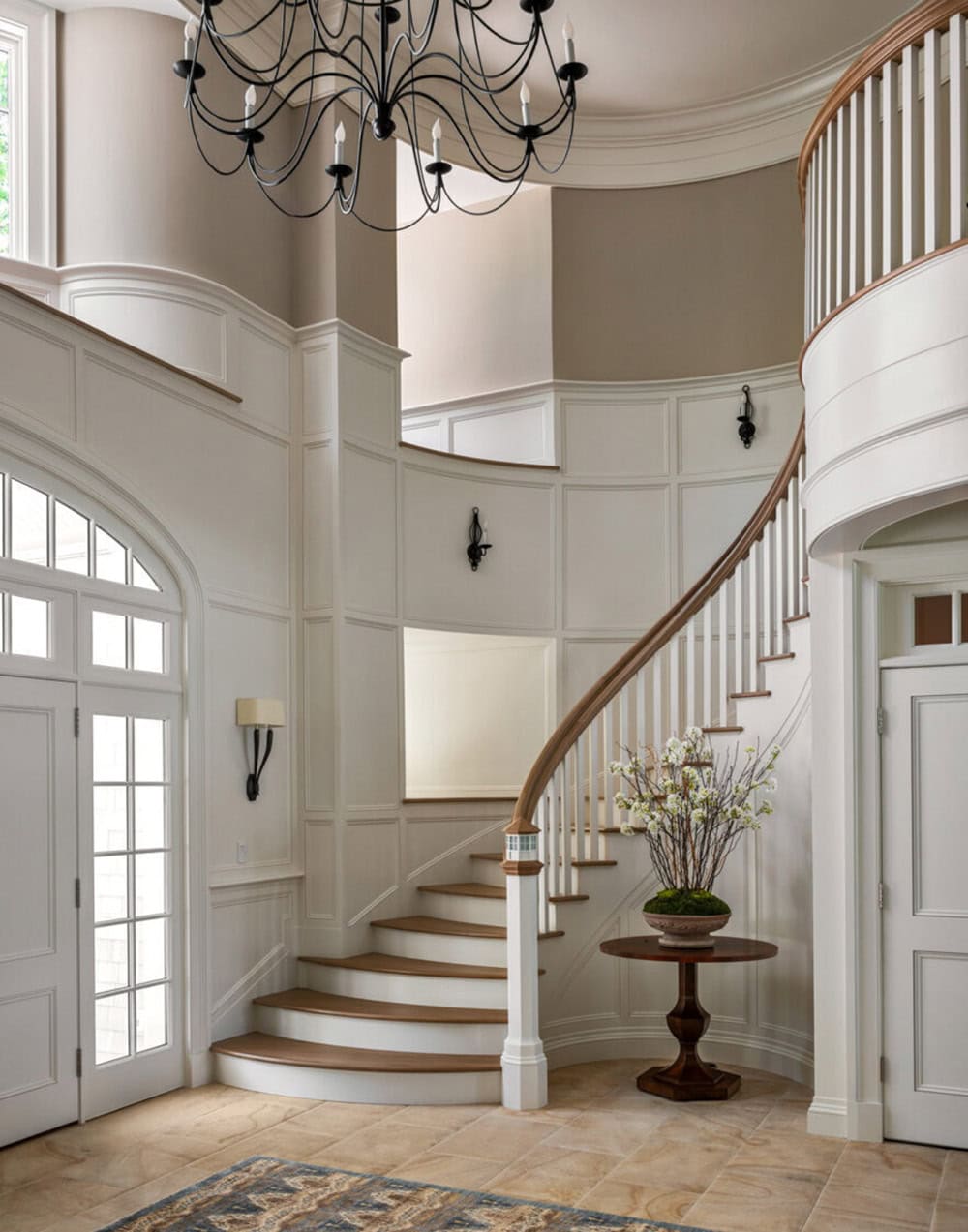 Curved staircase with wood railing beneath a wrought-iron chandelier in entry hall