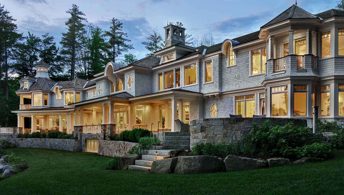 Twilight view of the home's long shingle-style facade with porches and turret lit from within