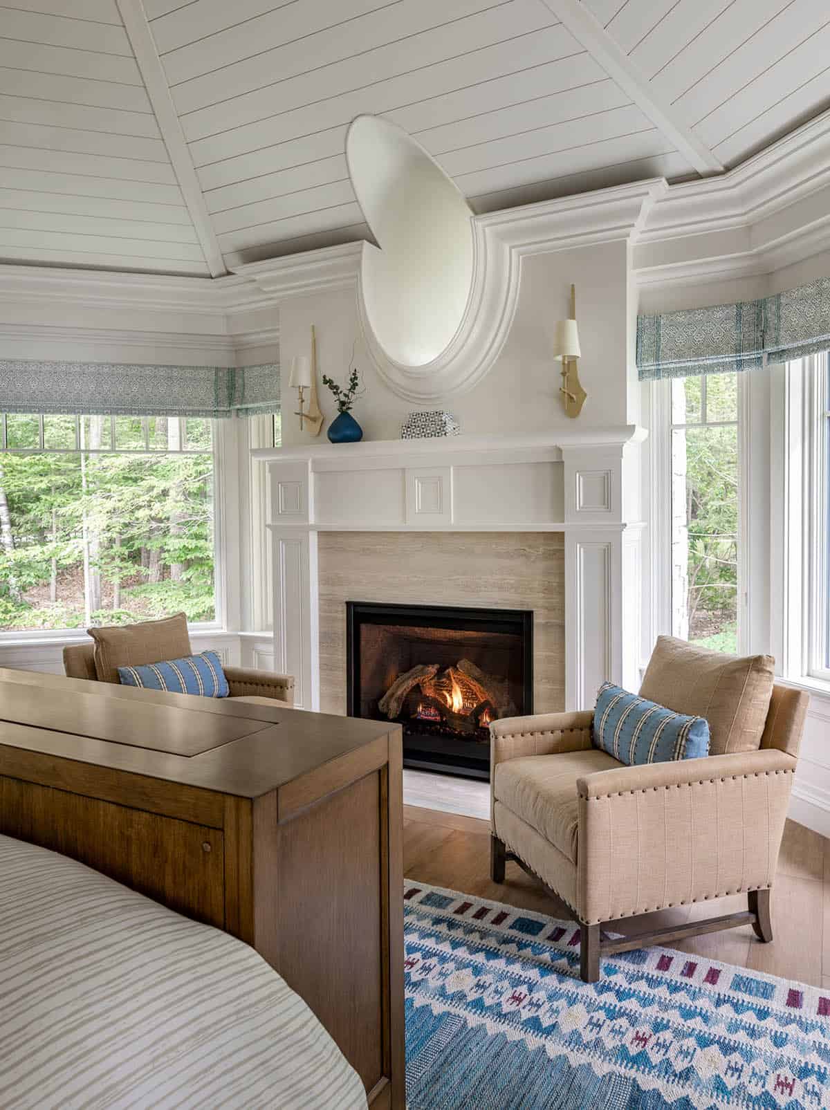 Primary bedroom seating area with oval mirror above stone fireplace and bay window