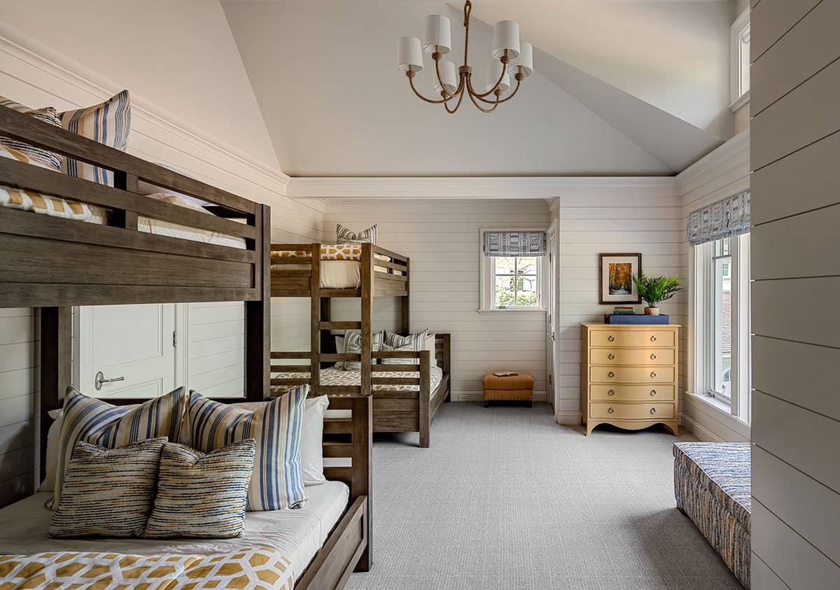 Bunk room with three wooden bunk beds, striped pillows, and yellow dresser