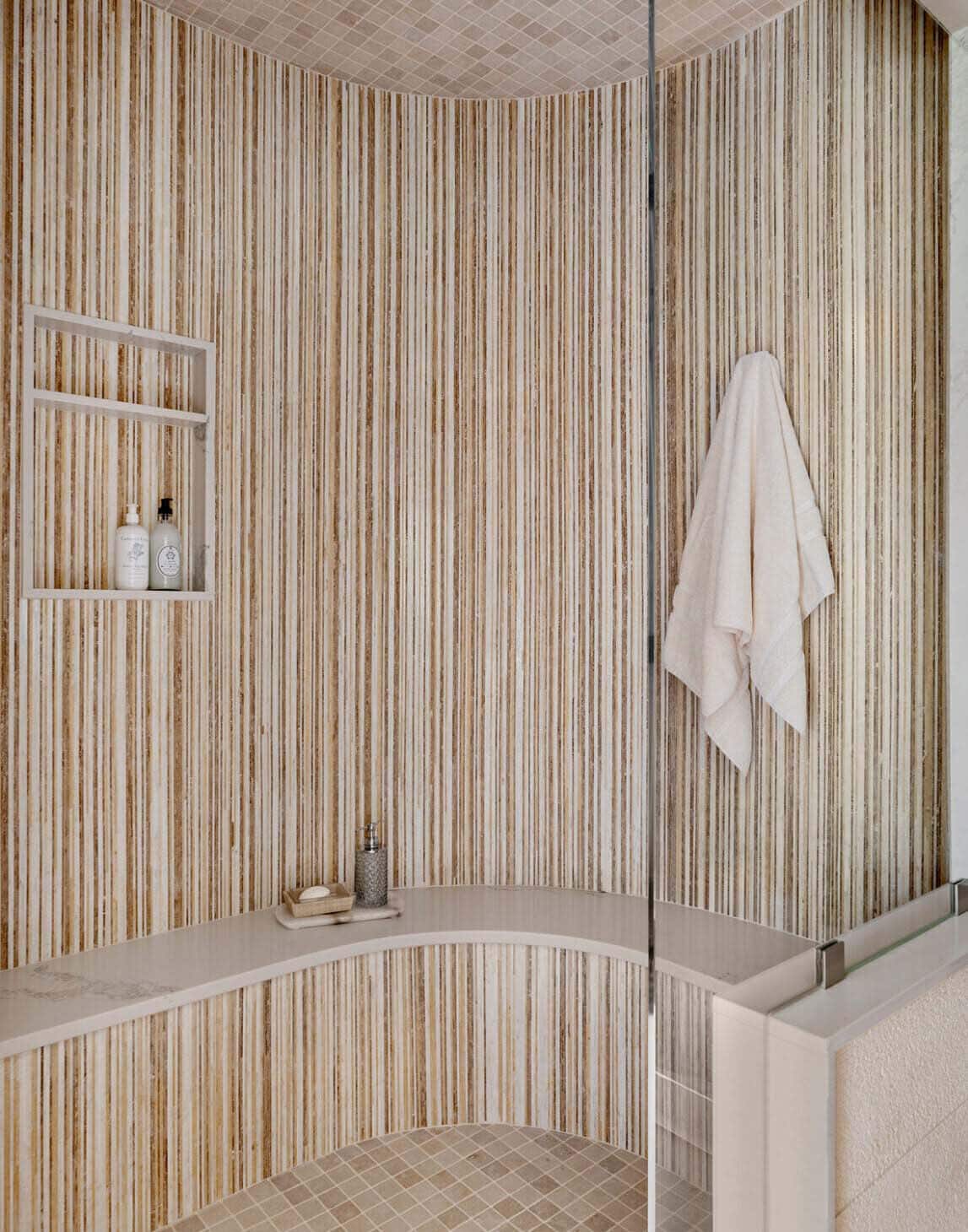 Curved shower with vertical reeded tile, built-in niche, and glass partition