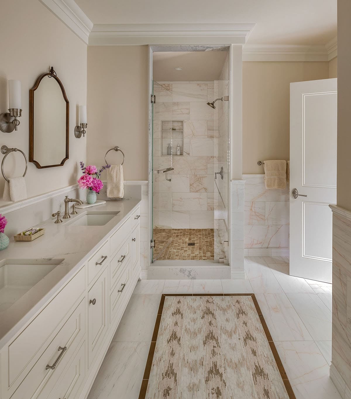 White marble bathroom with glass shower stall and patterned runner rug